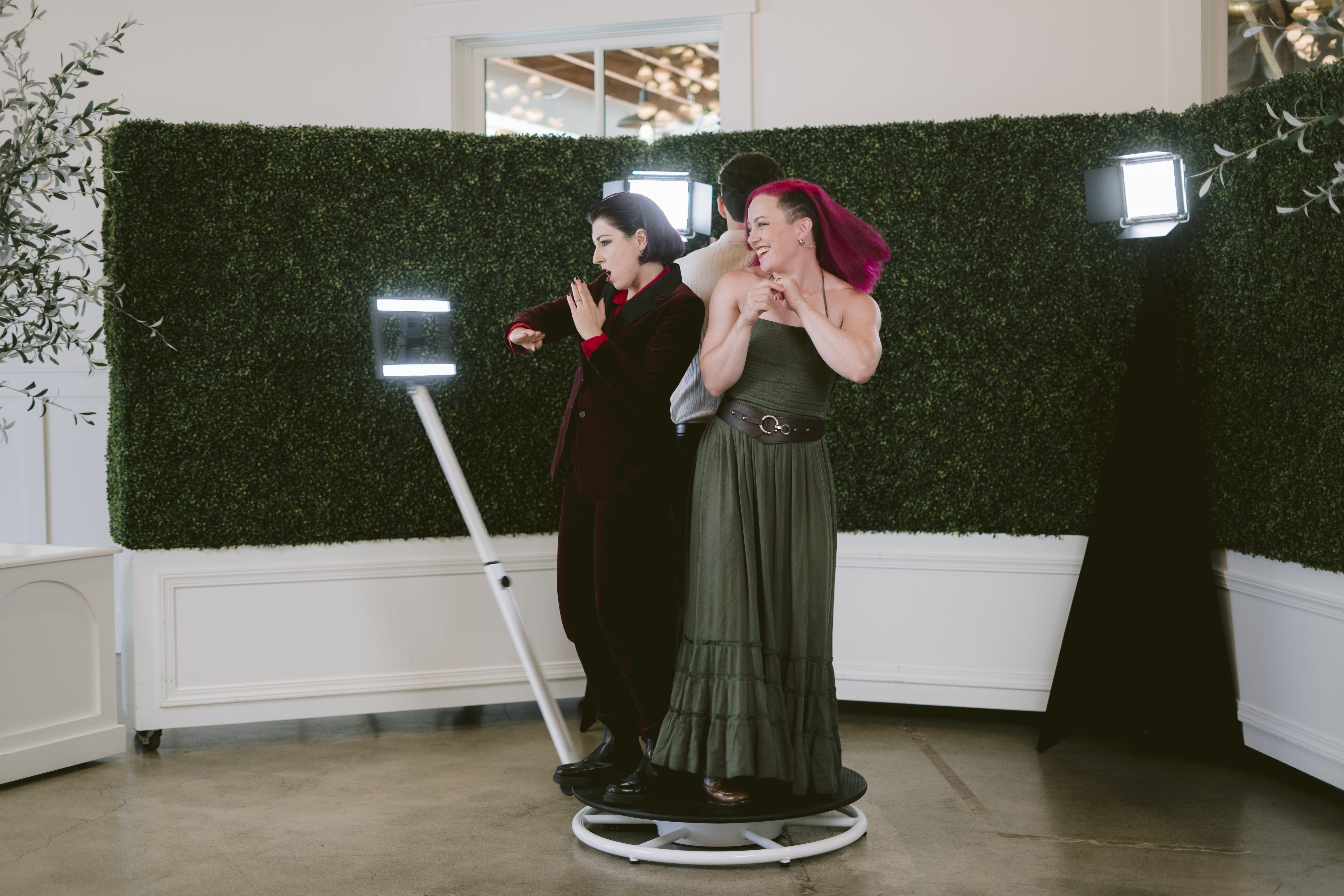Two guests posing on the 360 booth platform in front of a greenery wall