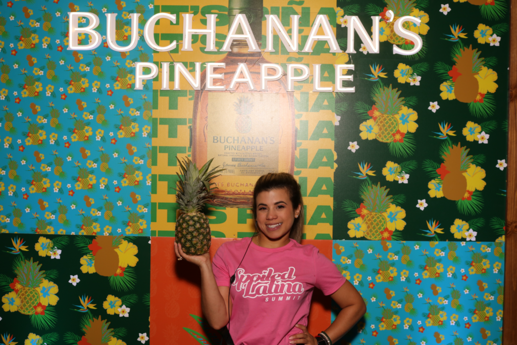 Guest holding a pineapple in front of the Buchanan's Pineapple neon backdrop