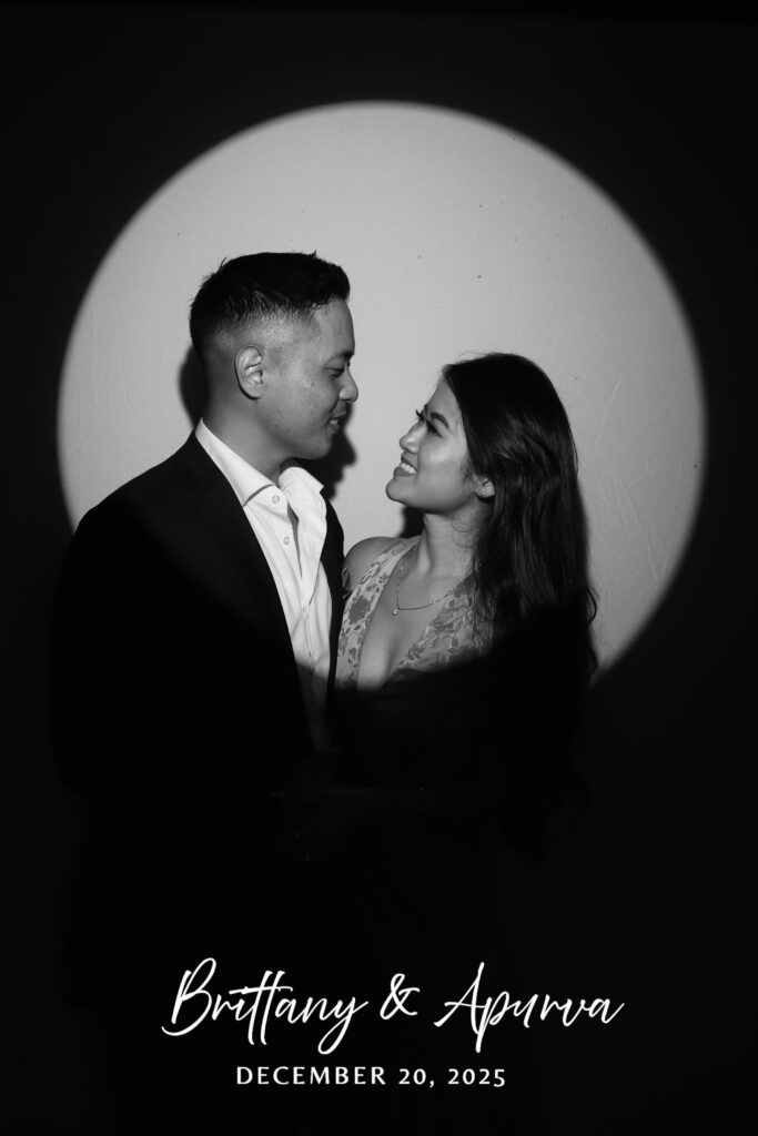 Black and white spotlight portrait of a couple in profile, smiling at each other