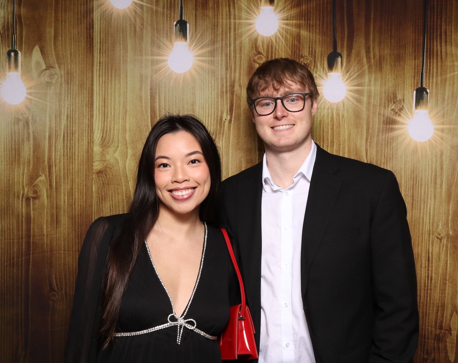 Two guests at a Houston corporate holiday party photo booth with a warm wood backdrop