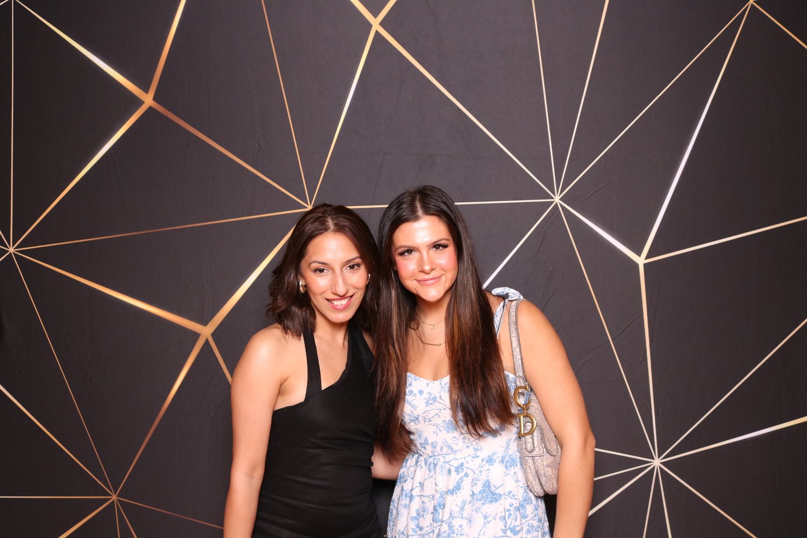 Two guests posing at a Houston event photo booth with a geometric backdrop