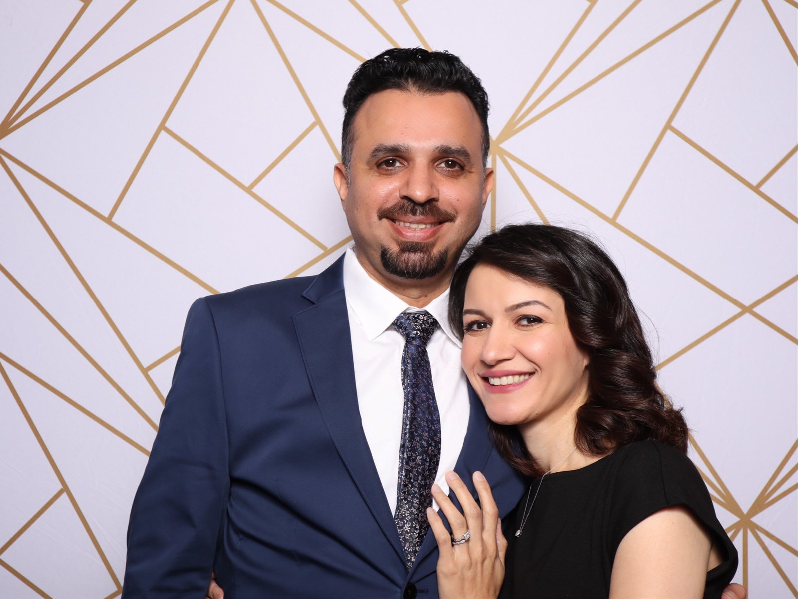 Couple at a Houston company holiday party photo booth with a white and gold geometric backdrop